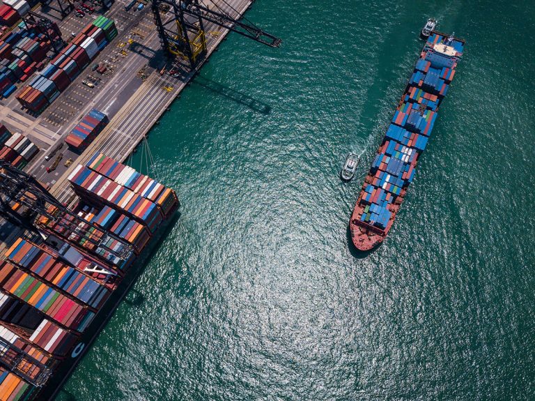 Aerial view of a cargo ship travelling with some containers beside a dock