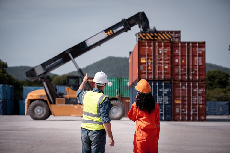 Two workers watching a crane move shipping containers